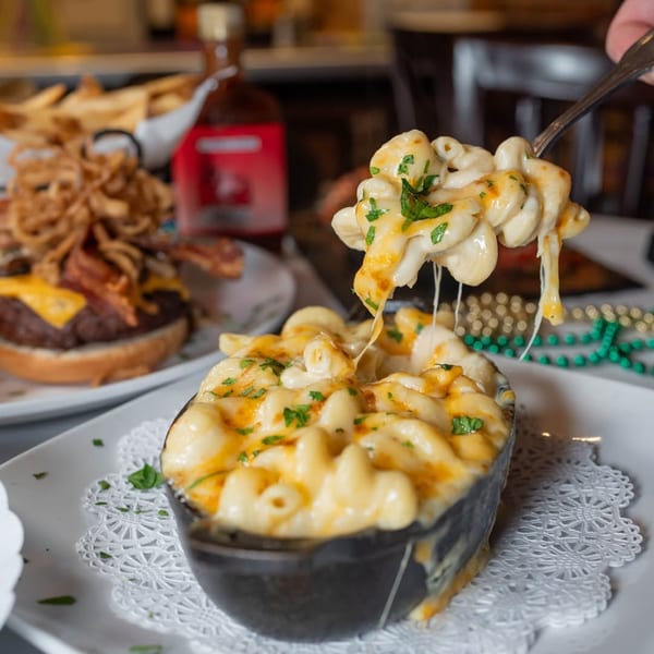 Cheesy mac and cheese in a cast iron bowl, with a spoonful lifted, alongside a burger.
