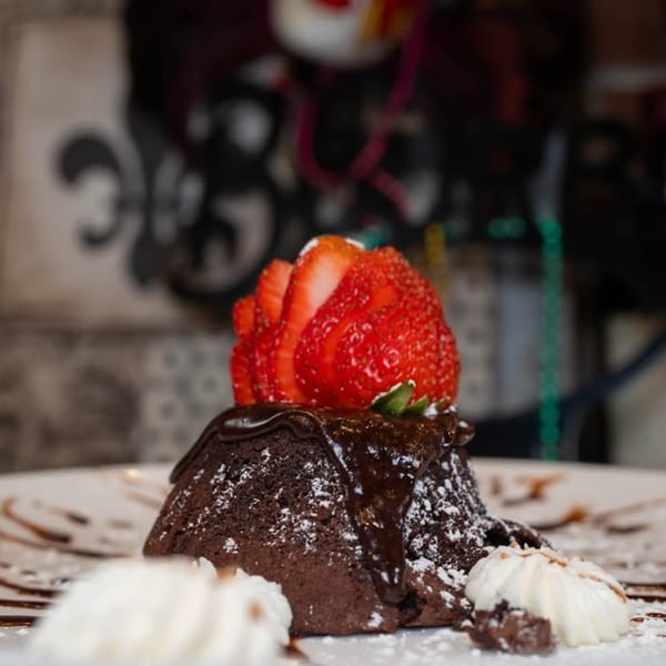 Chocolate lava cake with powdered sugar, chocolate drizzle, sliced strawberries, and whipped cream.