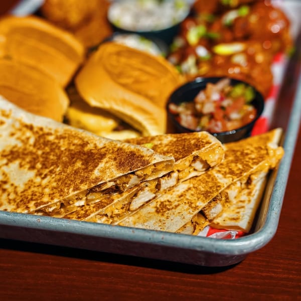A metal tray filled with quesadilla slices, sliders, and small bowls of salsa and other Cajun sides.