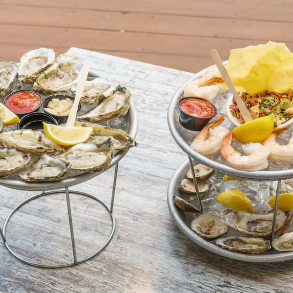 Two tiered seafood towers with oysters, shrimp, and clams on ice, with sauces and lemon wedges.