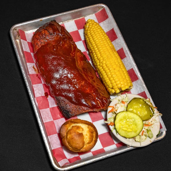 Bourbon Street's BBQ ribs, corn on the cob, cornbread, coleslaw, and pickles on a metal tray.