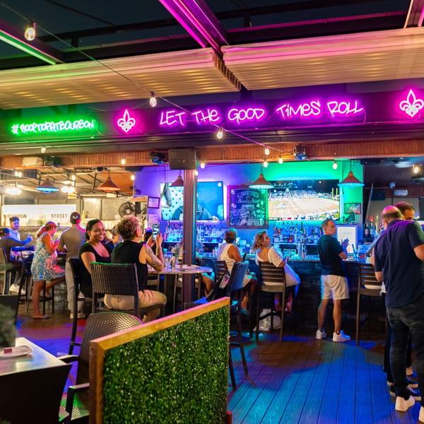 Patrons enjoying drinks at the Bourbon Street bar, illuminated by neon signs and string lights.