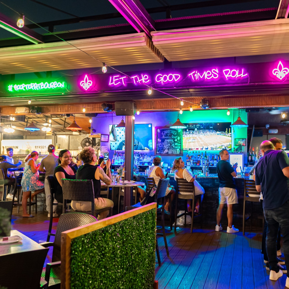 Patrons enjoying drinks at the Bourbon Street bar, illuminated by neon signs and string lights.