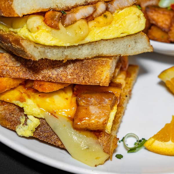 A close-up of a stacked breakfast sandwich with eggs, bacon, and melted cheese on toasted bread.